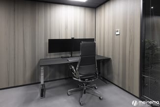 Moderne belcel met zwart bureau, ergonomische bureaustoel, dubbel monitor, toetsenbord en grijze vloer tegen houten wandafwer