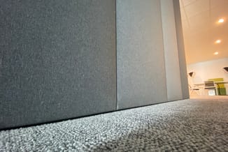 Grijze akoestische wandpanelen in kantoorruimte met tapijttegels, verlicht plafond met inbouwspots.
