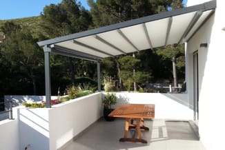 Moderne terrasoverkapping met witte aluminium frame en grijze zonneschermen boven houten tafel en wit terras.