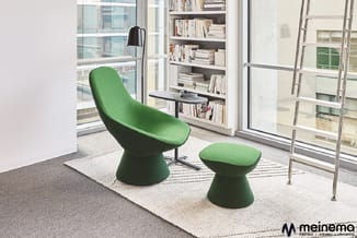 Groene loungestoel met bijpassende poef in moderne kantoorruimte met boekenkasten, ramen en zwart tafeltje.
