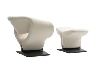 Twee witte stoelen met afgeronde vormen: een fauteuil met armsteunen en een voetenbankje, beide op zwart platform.