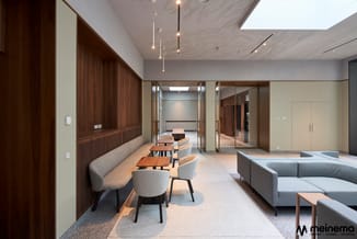 Modern kantoorinterieur met grijze banken, houten eettafel met grijze stoelen, houten wandbekleding en glazen deuren naar and