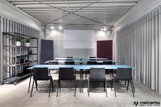 Moderne vergaderruimte met lichtblauwe tafel, zwarte stoelen, grijze verticale lamellen aan wanden, plafondverlichting en don