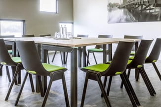 Moderne vergaderruimte met lichte houten tafel en zwarte stoelen met groen zitkussen, grote ramen en wandfoto.