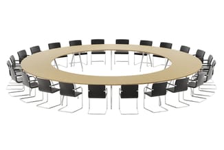 Grote ronde vergadertafel in licht hout met chromen onderstel, omringd door zwarte stoelen met metalen frame.