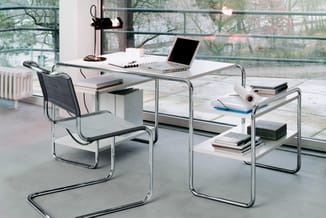Modern kantoorinterieur met wit bureau, metalen frame, zwarte mesh stoel, glazen zijmeubel met opbergruimte en grote ramen.