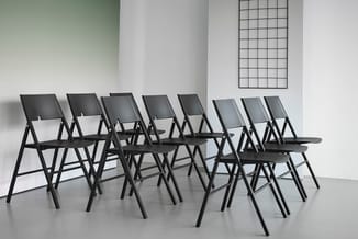 Acht zwarte klapstoelen met metalen frame en zitting in moderne kantoorruimte tegen witte wand.