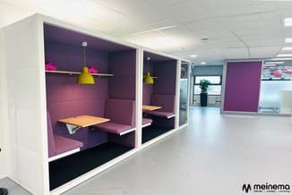 Twee paarse belcellen met witte frames, houten tafels, gele hanglampen en paarse zitbanken in een modern kantoor.