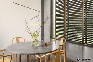 Ronde grijze vergadertafel met houten stoelen in minimalistisch interieur met betonnen zuil en gelamelleerde ramen.