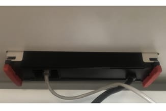 Zwarte ledstrip met rode eindkappen en grijs netsnoer, bovenaanzicht op witte ondergrond.