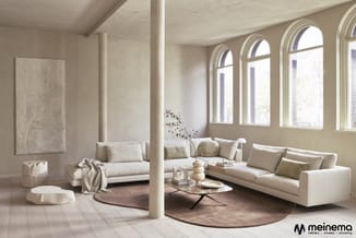 Moderne woonkamer met crèmekleurige banken, ronde tafel met stalen onderstel, houten vloer, grote raampartijen, zuilen en bei