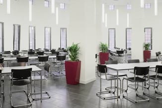Moderne kantoorruimte met witte tafels, zwarte bezoekersstoelen op wielen, rode plantenbakken en roestvrijstalen tafelpoten l
