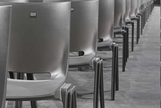 Rij witte kantoorstoelen met zwarte poten langs een grijze vloer, nummering "120" zichtbaar op achtergrond.