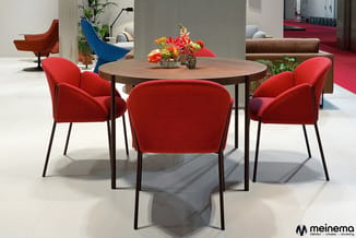 Ronde tafel met vier rode stoelen in moderne kantooromgeving met planten en bloemen.