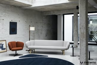 Moderne loungeset in betonnen loftruimte: grijze sofa met houten poten, rood-bruin fauteuil, donkerblauwe vloerkleed en staan