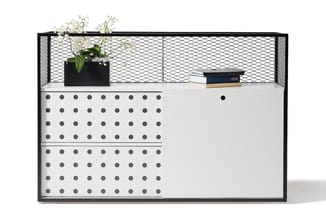 Wandkast met zwart metalen frame, witte planken en grijze pegboard-voorkant met gaten. Bovenop plant in zwarte pot en stapel