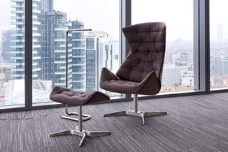 Bruine leren loungefauteuil met voetsteun in modern kantoor met panoramisch raamzicht op stedelijk skyline.