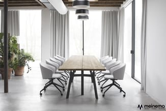 Moderne vergaderruimte met houten tafel, zwarte frame, grijze bureaustoelen op wieltjes, beige gordijnen, hanglamp, industrie