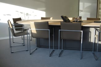 Moderne vergaderruimte met houten vergadertafel, zwarte stoelen met metalen frame en glazen wanden, natuurlijke verlichting.