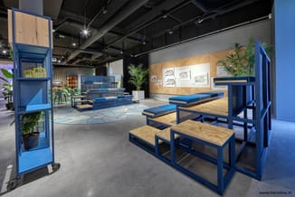 Moderne kantoorruimte met blauwe modulaire meubels, houten tafelbladen, blauwe zitbanken, legplanken met planten en illustrat