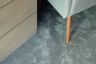 Grijze stoel met houten poot op grijs tapijt naast lichte houten vloer.