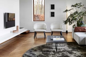 Moderne woonkamer met twee crèmekleurige stoelen, zwarte salontafel, houten vloer, grijze vloerkleed, TV-meubel, potplanten e