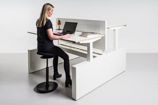 Vrouw aan witte bureau met laptop, zwarte bureaistoel, organizer en decoraties. Moderne kantoorinrichting.
