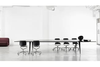 Lange vergadertafel met zwart blad en zwarte poten, omringd door zwarte bureaustoelen op wielen in minimalistisch wit kantoor