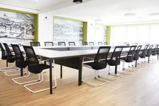 Moderne vergaderruimte met lange witte tafel, zwarte kantooorstoelen met witte poten, houten vloer en groene raamkozijnen met