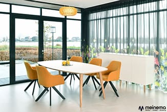Moderne vergaderruimte met ovale witte tafel, gele stoelen met zwarte poten, gouden hanglamp en groene raampartijen met uitzi