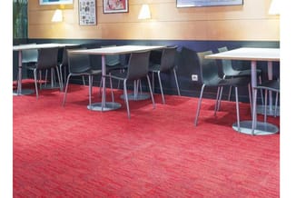 Kantoorruimte met zwarte stoelen aan witte rechthoekige tafels op rood tapijt, houten wandafwerking en wandverlichting.