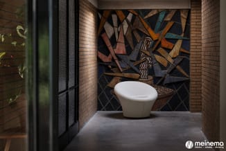 Witte ronde fauteuil in minimalistisch interieur met bakstenen muren en abstract mozaïekkunstwerk in warme en koude tinten.