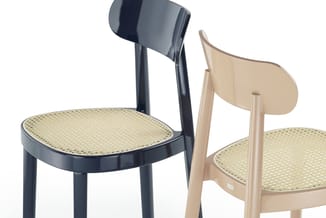 Twee stoelen met rotan zitting: één zwart met gebogen rugleuning, één natuurkleurig hout met ovale rugleuning.