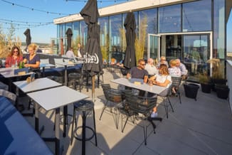 Dakterras met zwarte parasols, witte tafels, zwarte ergonomische stoelen en loungebanken. Moderne glazen gebouw met uitzicht