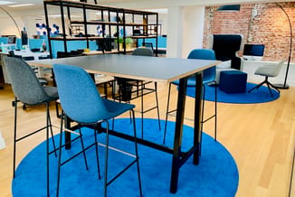 Moderne kantoorinrichting met grijs statafel op zwart onderstel, blauwe barstoeien, blauwe ronde tapijten op houten vloer, ba