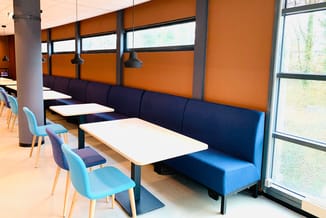 Moderne kantoorinrichting met blauwe zitbank, witte tafels, lichtblauwe stoelen en oranje akoestische wandpanelen tegen grote
