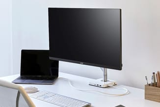 Werkplek met laptopcomputer, externe monitor op zilverkleurige standaard, draadloos toetsenbord en muis op wit bureau. Houten