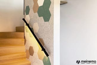 Trappenhuiswand met grijs en groen hexagonaal akoestiekpanelensysteem, houten treden en zwarte trapleuning.