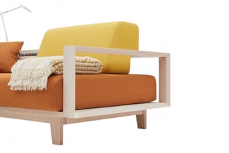Moderne houten fauteuil met oranje zitting, gele rugleuning en crèmekleurig plaid en kussen.