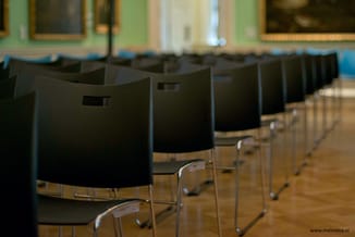 Rij zwarte kunststof stoelen met metalen frame in vergaderruimte met houten vloer en groene muurverf.