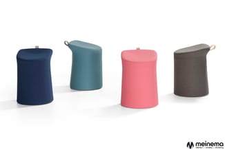 Vier cilindervormige poefs in donkerblauw, grijs-blauw, roze en grijs met beige hengsels, gerangschikt op witte ondergrond.