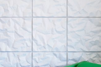 Groen modern zitmeubel tegen witte tegelmuur met geometrisch patroon.