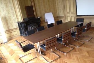 Vergadertafel in donker hout met zwarte stoelen met houten armleuningen in klassieke kantoorruimte met open haard.