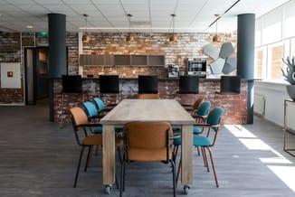 Moderne kantoorruimte met lichte houten vergadertafel, bruine en blauwe stoelen, bakstenen wand, hangende koperen lampen en t