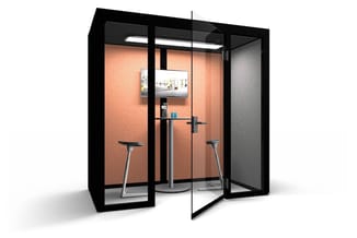 Akoestische belcel met zwart frame, oranje akoestische wandbekleding, twee zithoogtabourets, staanwerkplek, monitor en overhe