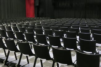 Zwarte moderne stoelen in rijen opgesteld in een theater of conferentiezaal met rode gordijn op de achtergrond.