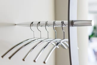 Rij zilveren garderobe-hangers op zilverkleurige staaf tegen witte wand in kantoor.