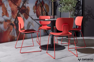 Rode kunststof stoelen met rode buisframe rond zwarte ronde tafel op terras met herfstbladeren.