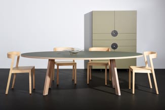 Ovale vergadertafel met grijs blad en houten poten, omringd door houten stoelen, achter een groenachtig kastenstelsel met klo