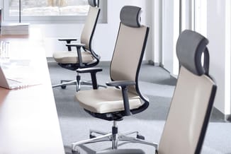 Kantoorruimte met drie ergonomische bureaustoel in beige en grijs, zwarte armsteunen, op grijs tapijt. Wit bureau links, grot